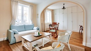Un salon chaleureux avec un canapé, une table en bois, des chaises en osier et une grande porte en arc donnant sur un placard.