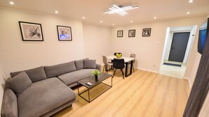Un salon moderne avec un canapé gris, une table basse agrémentée d’une plante, et un coin repas comprenant une table et des chaises.