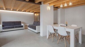 A modern interior with a white sofa, a dining table with chairs, and wooden ceiling beams.