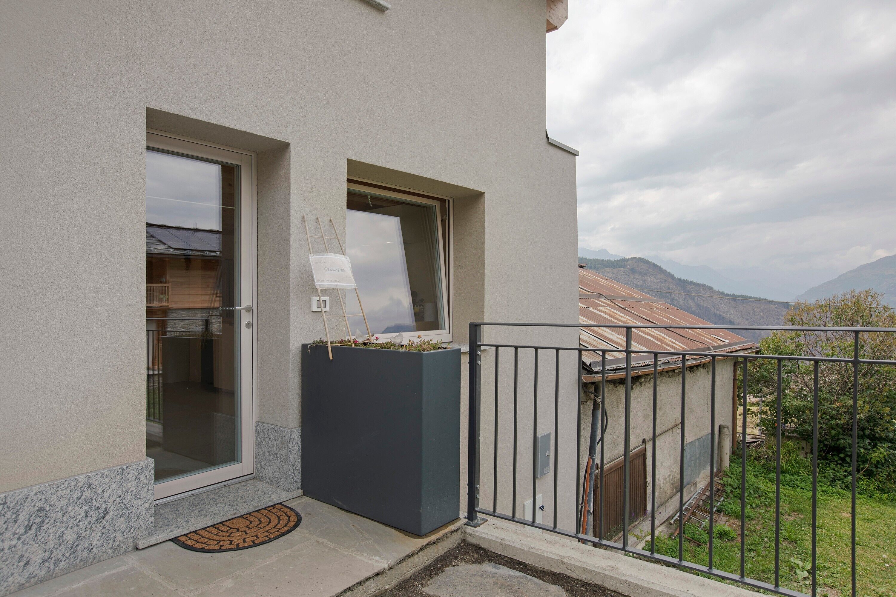 Ein Balkon mit Bergblick, eine Tür mit Glasfenster und ein kleines Fenster mit Staffelei.