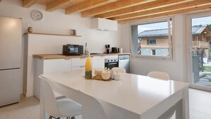 A modern kitchen with wooden beams, a white countertop, and a dining area with a white table and chairs.