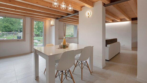 A modern interior with a wooden ceiling, large windows, a dining table with chairs, and a sofa.