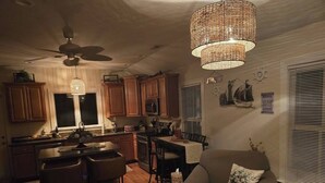 A cozy kitchen with wooden cabinets, a dining area with a chair and ottoman, and a ceiling fan. - Downtown Riverside Lighthouse (New Bern)