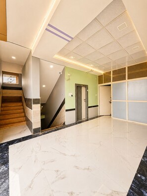 Un interior moderno con piso de mármol, una escalera y una pared de acento verde.