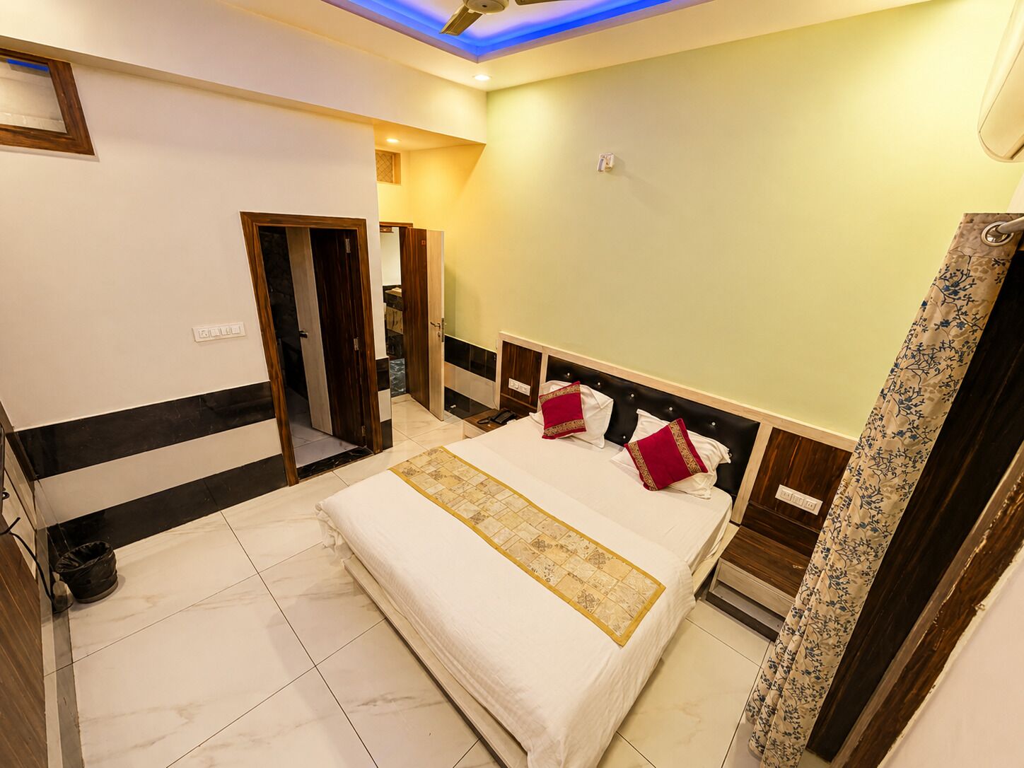 Une chambre d’hôtel avec un lit, un ventilateur de plafond, un luminaire et une porte.