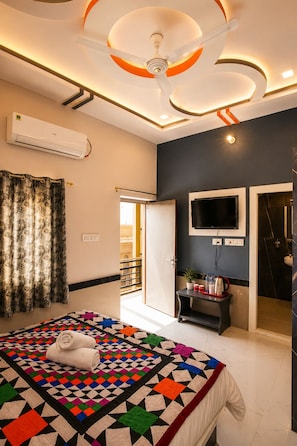A hotel room with a bed, a TV mounted on the wall, a small table with a plant, and an air conditioning unit. - Hotel The Vintage Villa Jaisalmer (Jaisalmer)