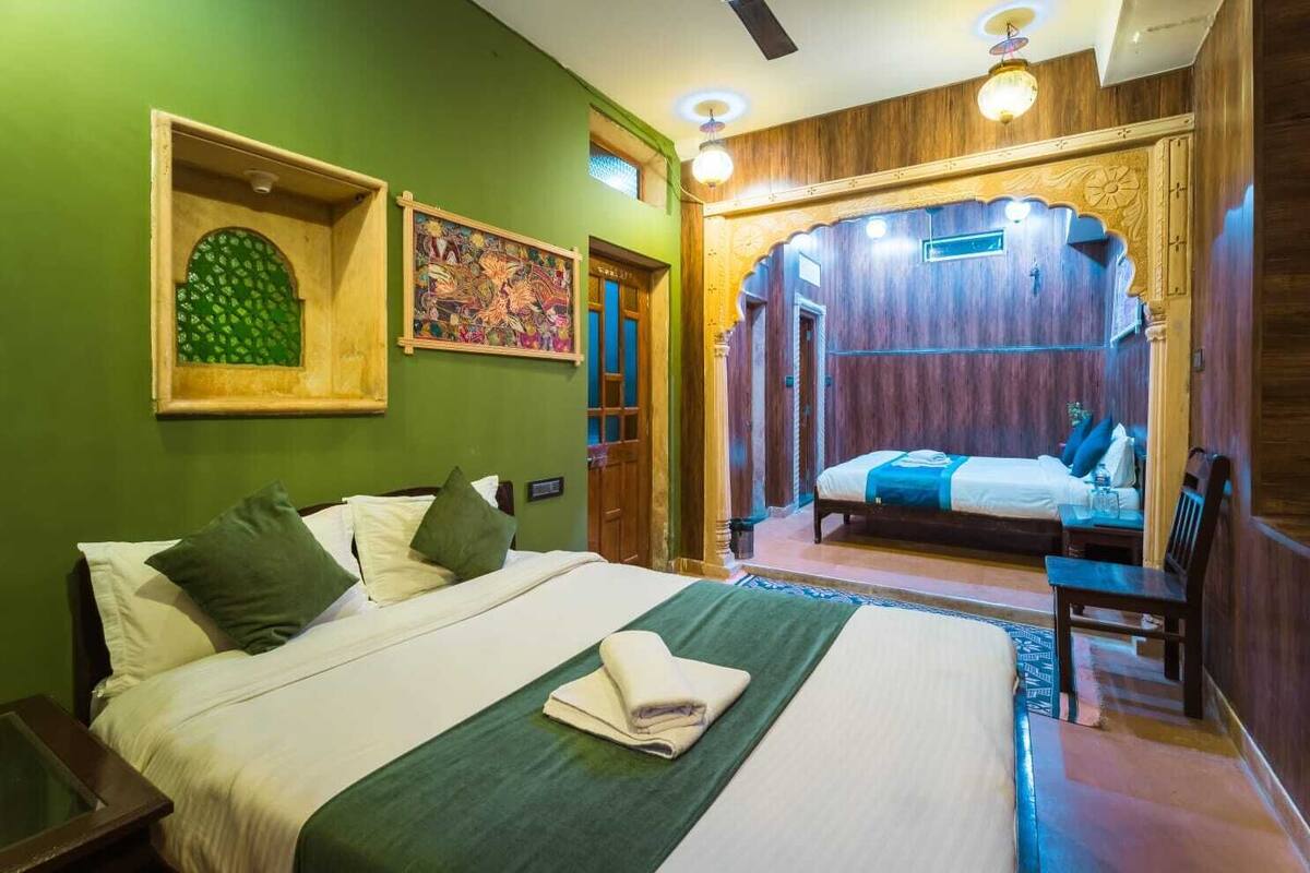 Ein Hotelzimmer mit einem großen Bett, einem Schreibtisch und einem Stuhl. Eine Tür führt in einen weiteren Raum.