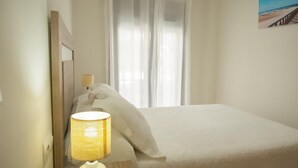 A hotel room with a bed, a lamp, a window with curtains, and a painting on the wall. - Apartment in the City Center (Conil de la Frontera)