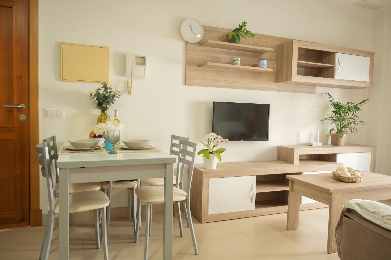Una sala de estar moderna con una mesa de comedor, sillas, un televisor y estanterías empotradas con objetos decorativos.