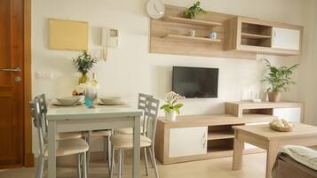 Una sala de estar moderna con una mesa de comedor, sillas, un televisor y estanterías empotradas con objetos decorativos.