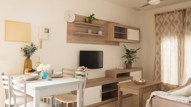 A modern living room with a dining area, a flat-screen TV, wooden shelves, and a ceiling fan. - Apartment in the City Center (Conil de la Frontera)