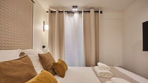 A hotel room with a bed, pillows, a towel rack, and a window with curtains. - Superb Apartment Center of Paris by Studio Prestige (Paris)