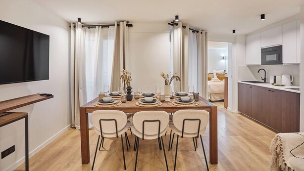 A modern dining area with a wooden table set for four, flanked by cream-colored chairs. A flat-screen TV is mounted on the wall to the left. - Superb Apartment Center of Paris by Studio Prestige (Paris)