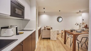 A modern kitchen with a built-in oven and microwave, a dining area with a wooden table and chairs, and a sofa in the background. - Superb Apartment Center of Paris by Studio Prestige (Paris)