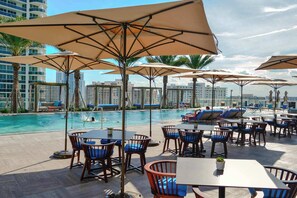 A rooftop pool area with lounge chairs, umbrellas, and tables. - 1BR Beach Condo | Sea View | Hollywood Broadwalk (Hollywood)