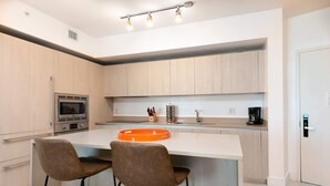 A modern kitchen with a central island, stainless steel appliances, and two bar stools. - 1BR Beach Condo | Sea View | Hollywood Broadwalk (Hollywood)