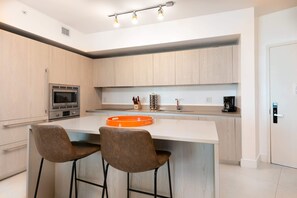 A modern kitchen with a central island, stainless steel appliances, and two bar stools. - 1BR Beach Condo | Sea View | Hollywood Broadwalk (Hollywood)