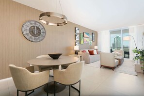 A modern living room with a dining area, featuring a round table, chairs, a large wall clock, and artwork. - 1BR Beach Condo | Sea View | Hollywood Broadwalk (Hollywood)