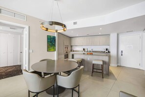 Une cuisine moderne dotée d’un îlot central, d’un coin repas avec une table ronde et des chaises, et d’un grand luminaire suspendu.