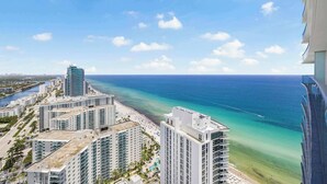 A high-rise hotel overlooking a beach with clear blue water and a distant city skyline. - Roomy 2BR | Beach + Pool | Sleeps 6 (Hollywood)