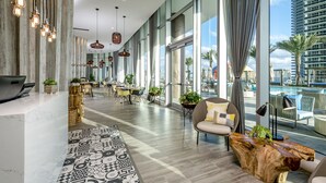 A modern hotel lobby with a large seating area, a pool view, and a mix of natural and artificial lighting. - Roomy 2BR | Beach + Pool | Sleeps 6 (Hollywood)