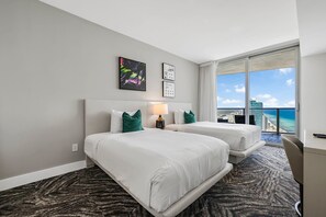 Une chambre d’hôtel avec deux lits, un bureau, une vue sur l’océan et un panorama sur la ville.