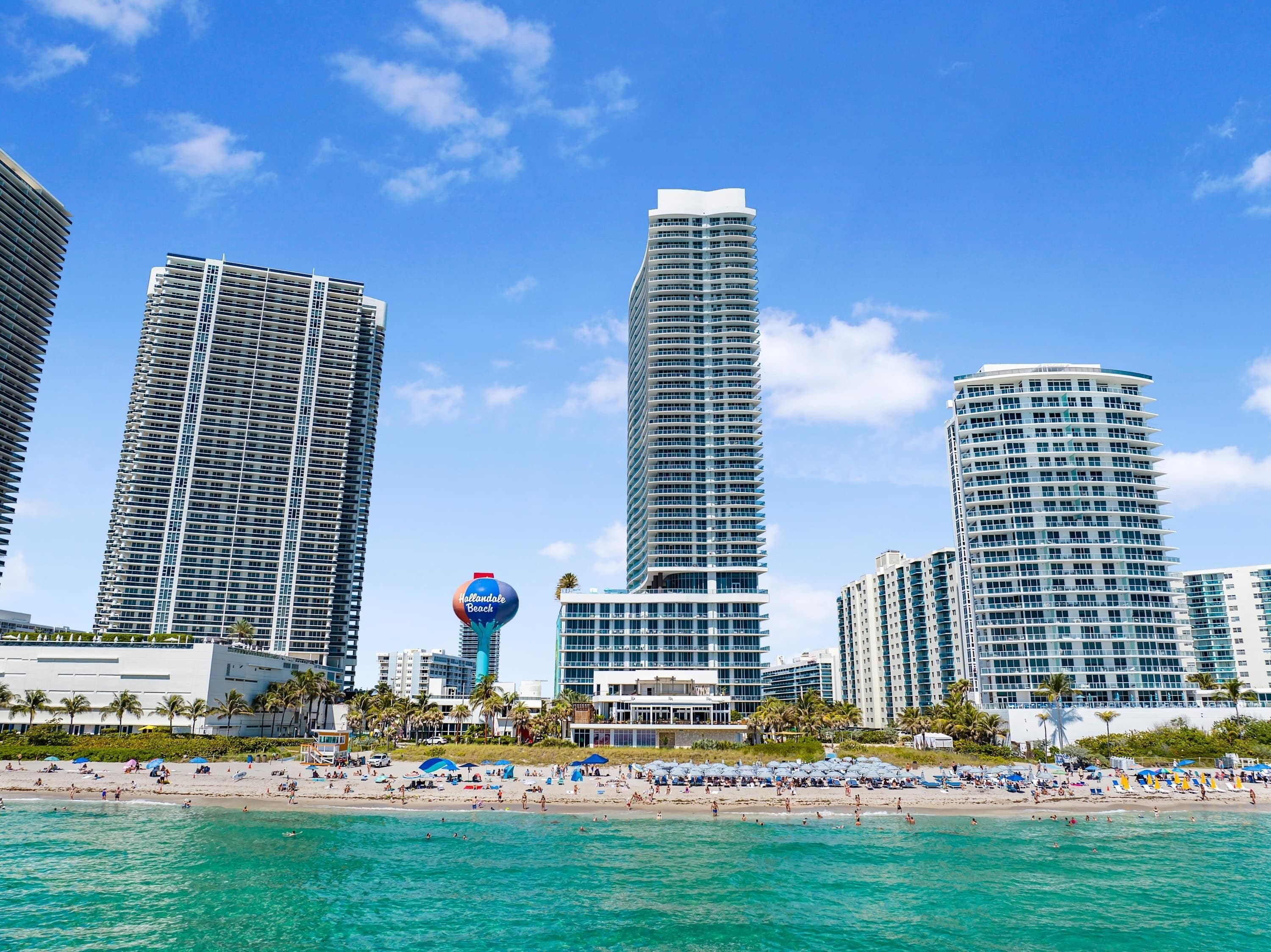 A beachfront hotel with high-rise buildings, a beach, and a clear sky.