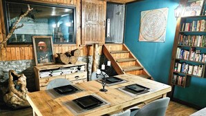 Un cuarto acogedor con una mesa de madera, sillas, una estantería, una escalera y un amplio ventanal.