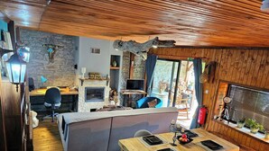 Acogedor interior de cabaña con chimenea de piedra, techo de madera y comedor con mesa dispuesta para cuatro.