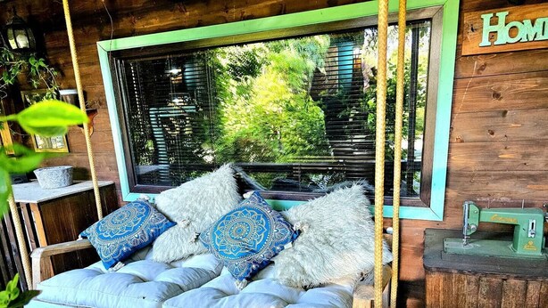 Una hamaca de madera con vistas a follaje, una máquina de coser y un letrero que dice 'Home'.