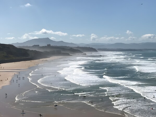 Una playa con olas, gente y montañas a lo lejos.