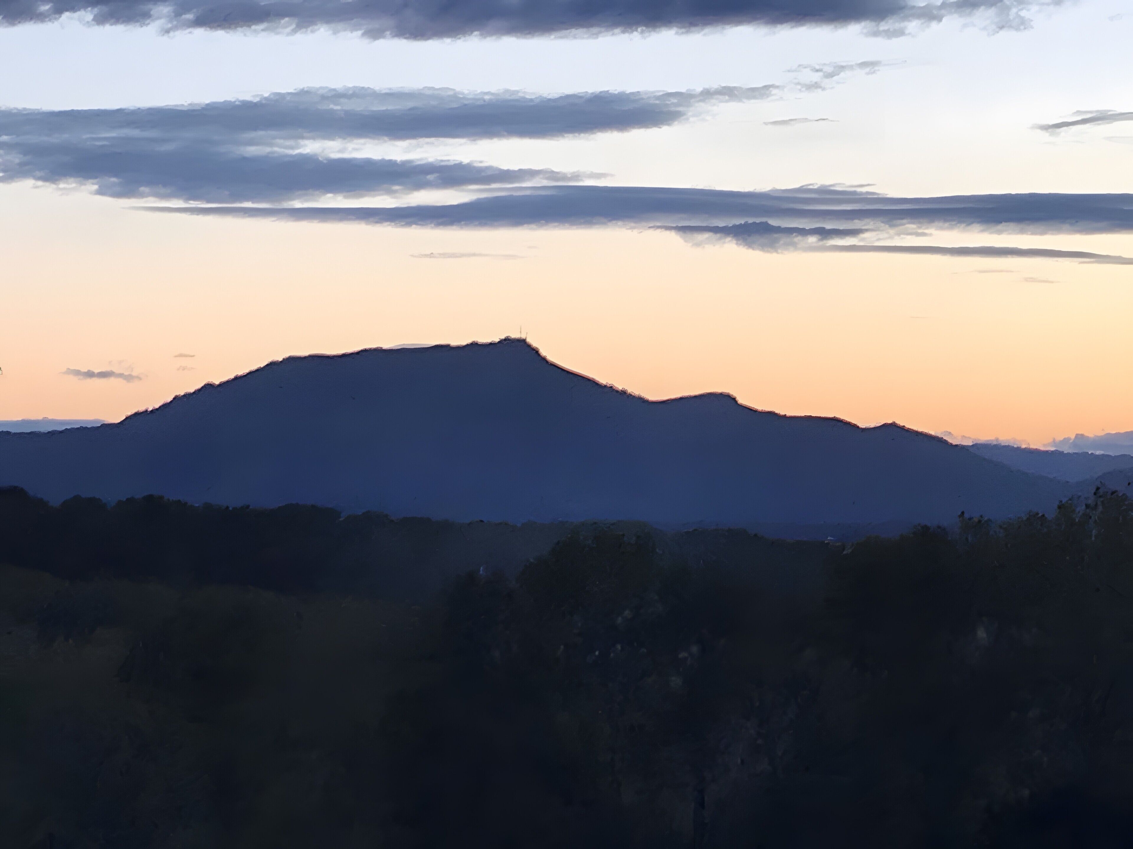 A mountain silhouette against a sky with clouds.