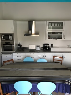 Una cocina moderna con microondas, horno y cafetera. Hay dos sillas y una mesa de comedor.