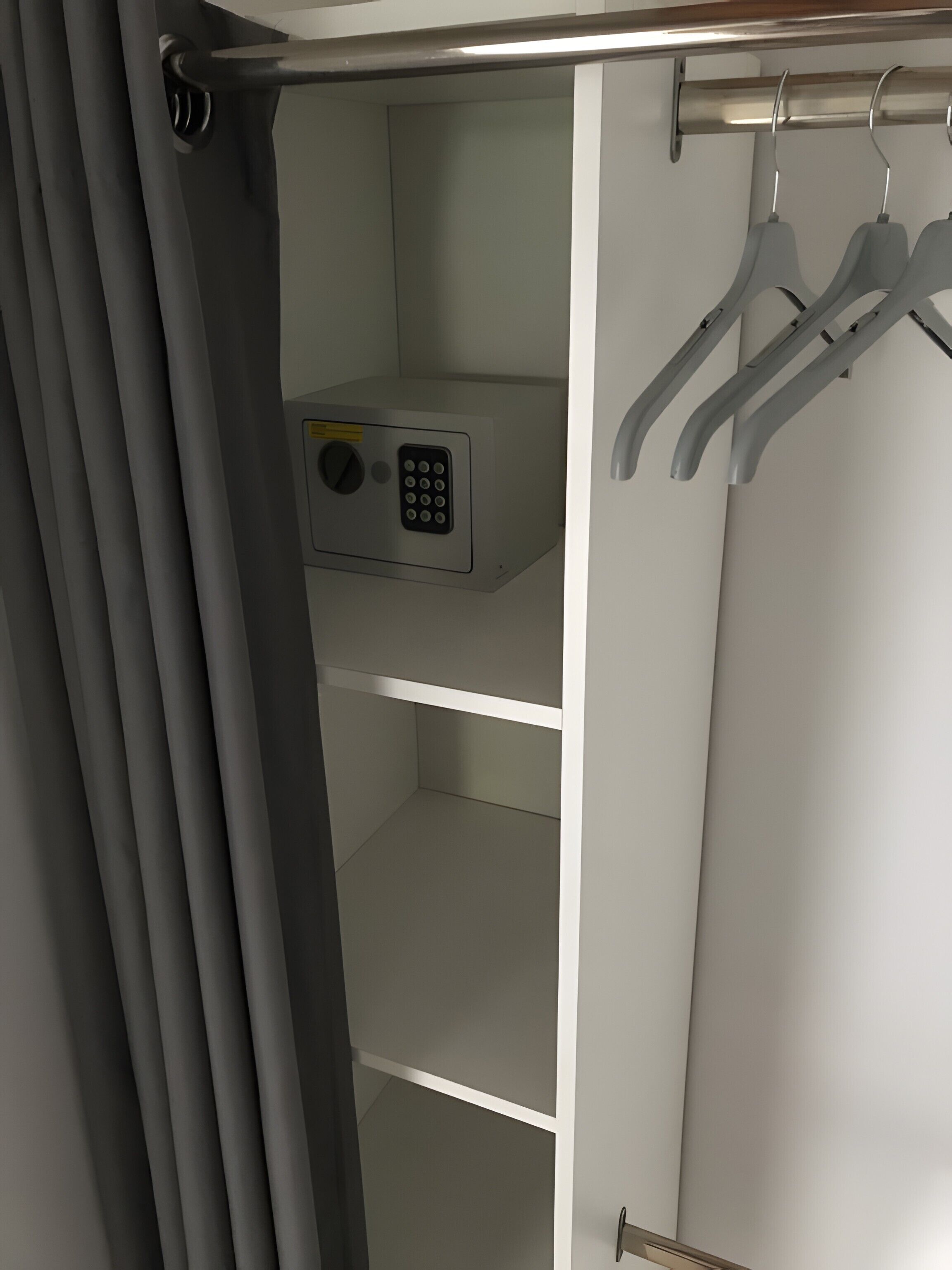 A white wardrobe with a microwave on the top shelf, a hanging rod, and a door with a handle.