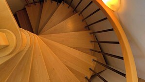 A wooden spiral staircase with a handrail and a light fixture on the wall. - Sunflower House (Bolzano)