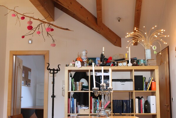 A room with a wooden ceiling, a bookshelf filled with books and decorative items, a candelabra, and a branch with pink flowers. - Maison Tournesol (Bolzano)