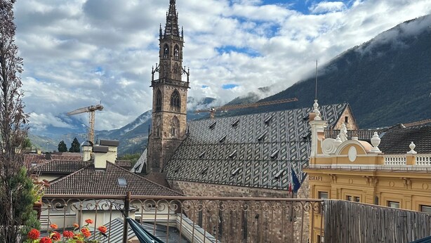 A rooftop terrace with a hammock, dining table with plates and glasses, and a view of a historic church and mountains. - Sunflower House (Bolzano)