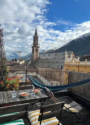 A rooftop terrace with a hammock, dining table with plates and glasses, and a view of a historic church and mountains. - Maison Tournesol (Bolzano)