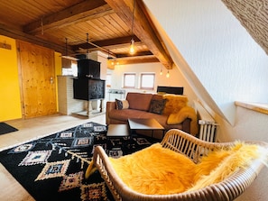 A cozy living room with a sofa, a wicker chair, a patterned rug, and a fireplace.