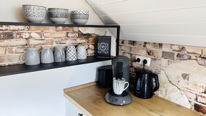 A kitchen with a brick wall, a coffee machine, and various mugs and bowls on a shelf.