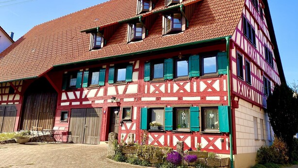 A traditional half-timbered building with a red roof, multiple windows, and a large wooden door.