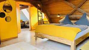A bedroom with a wooden ceiling, a bed with a yellow cover, two blue pillows, and a circular mirror on the wall.
