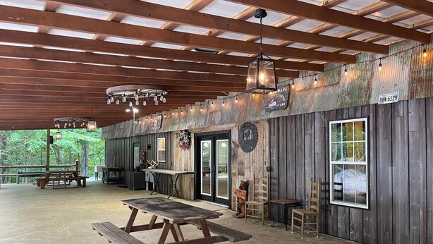 Une terrasse extérieure couverte, dotée de bancs en bois, de tables de pique-nique et de guirlandes lumineuses.