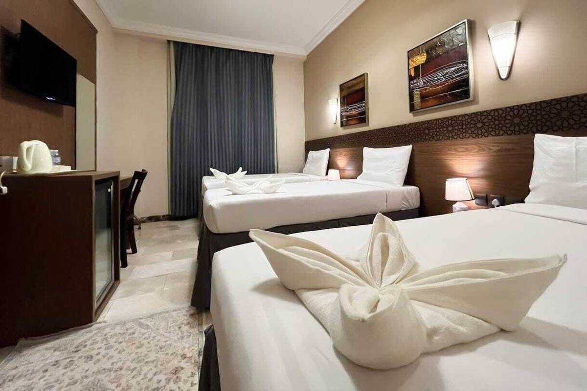 Ein Hotelzimmer mit zwei Betten, einem Schreibtisch, einem Fernseher und Bildern an den Wänden.