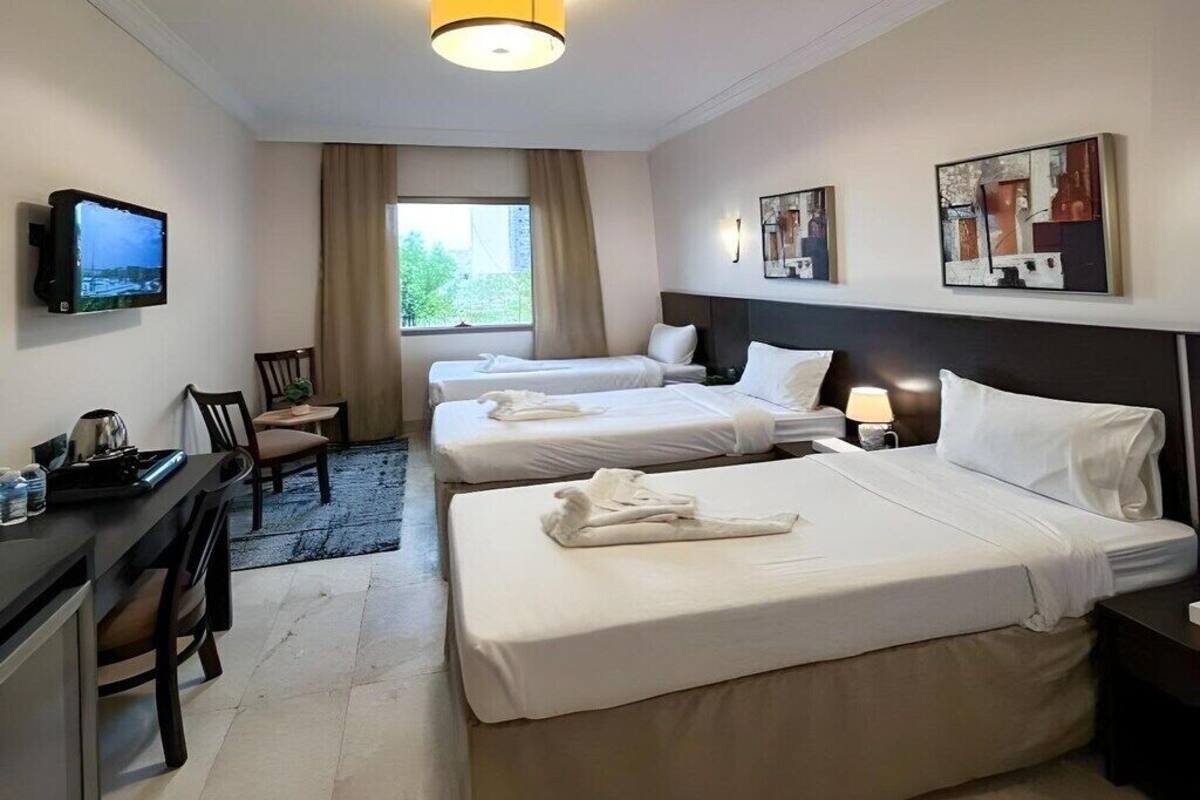 Ein Hotelzimmer mit zwei Betten, einem Schreibtisch mit Stuhl, einem Fernseher und Kunstwerken an den Wänden.