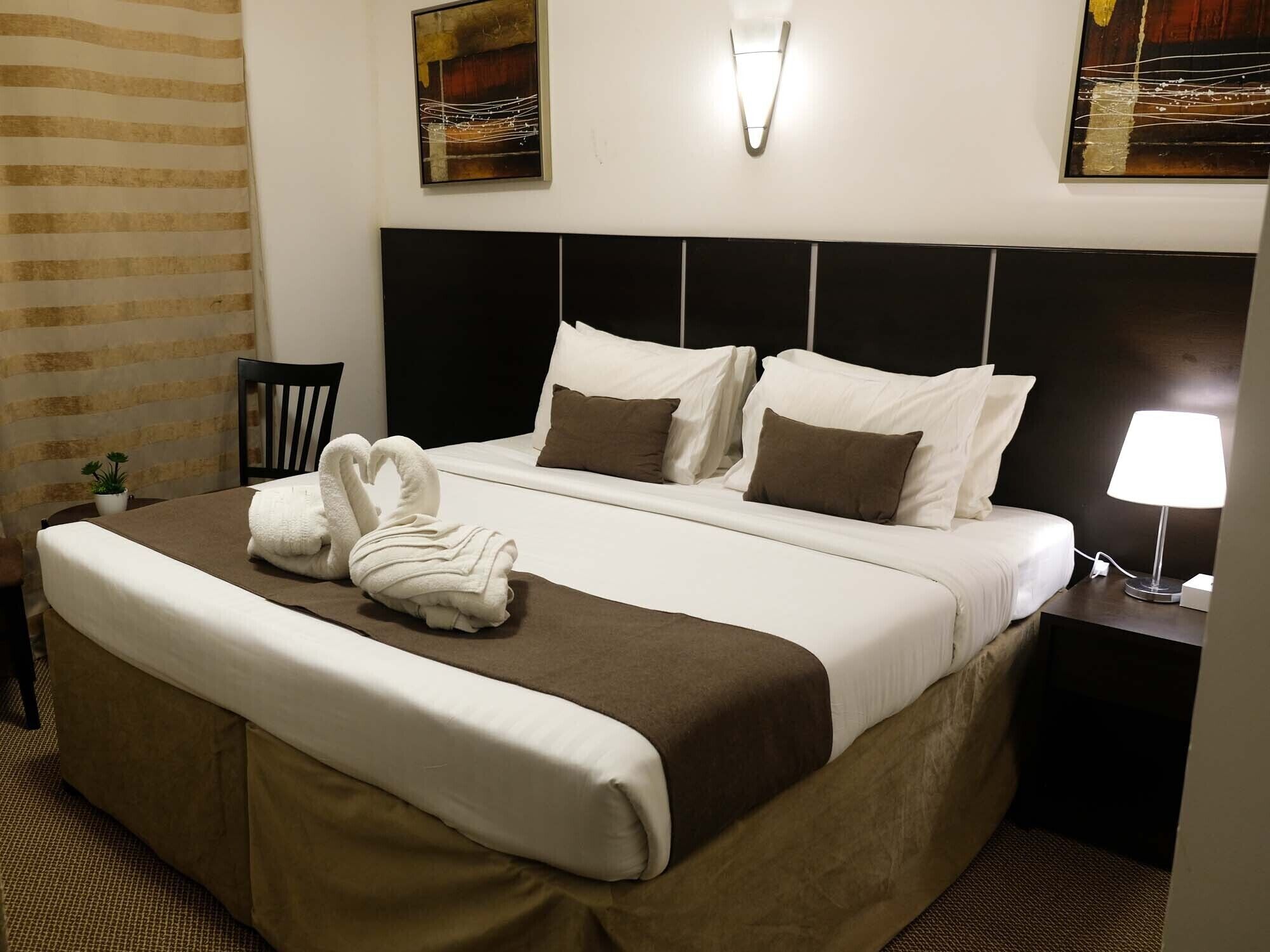Una cama bien hecha con ropa de cama blanca y marrón, un cabecero y una lámpara de noche.
