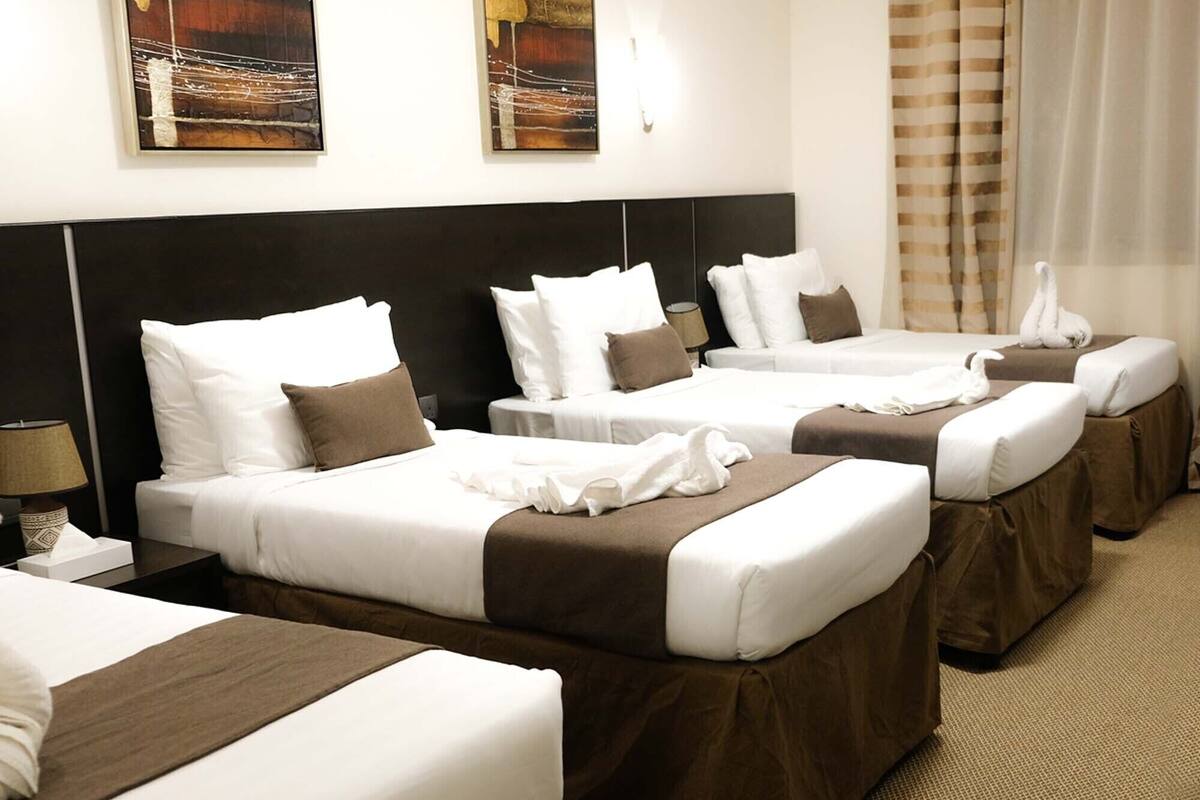 Ein Hotelzimmer mit vier Betten, die nebeneinander liegen, jeweils mit weißer Bettwäsche und braunen Kopfteilen.