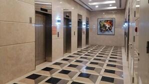 Een modern liftgedeelte met een zwart-wit schaakbordpatroon, meerdere liften en een groot abstract schilderij aan de muur.