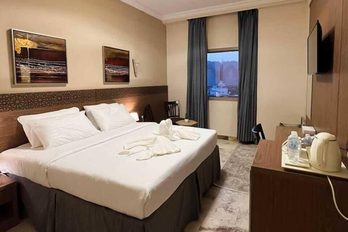 Ein Hotelzimmer mit einem großen Bett, einem Schreibtisch mit Stuhl, einem Fernseher und einem Fenster mit Vorhängen.