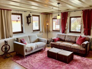 A living room with a sofa, a patterned couch, a rug, a vintage suitcase, and a wall clock.